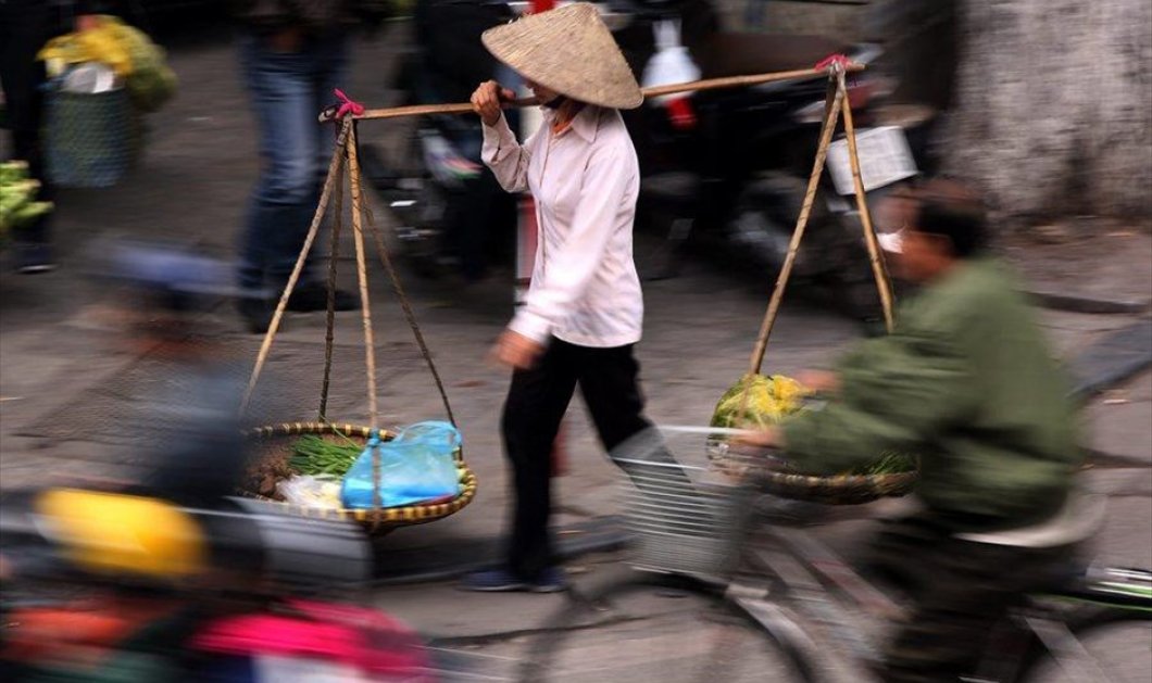 Στιγμιότυπο γεμάτο χρώμα: Πωλήτρια λουλουδιών περπατά σε δρόμο του Ανόι, στο Βιετνάμ - EPA / LUONG THAI LINH