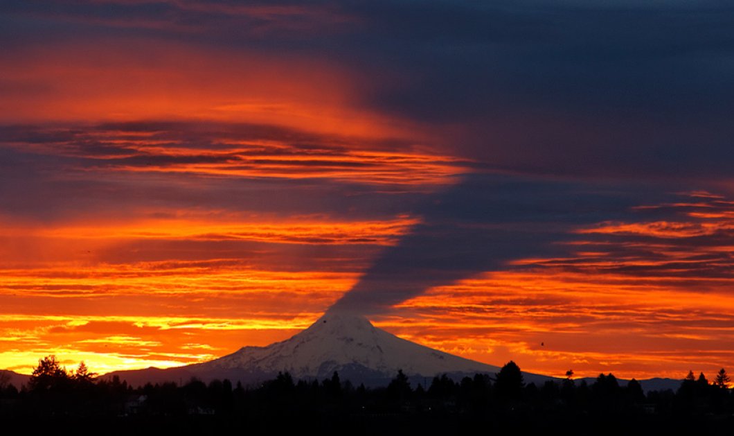 Σαν σκιά μοιάζει το Mount Hood όταν ο ήλιος δύει στα σύννεφα κοντά στο Portland - Picture: Mike Zacchino/The Oregonian via AP