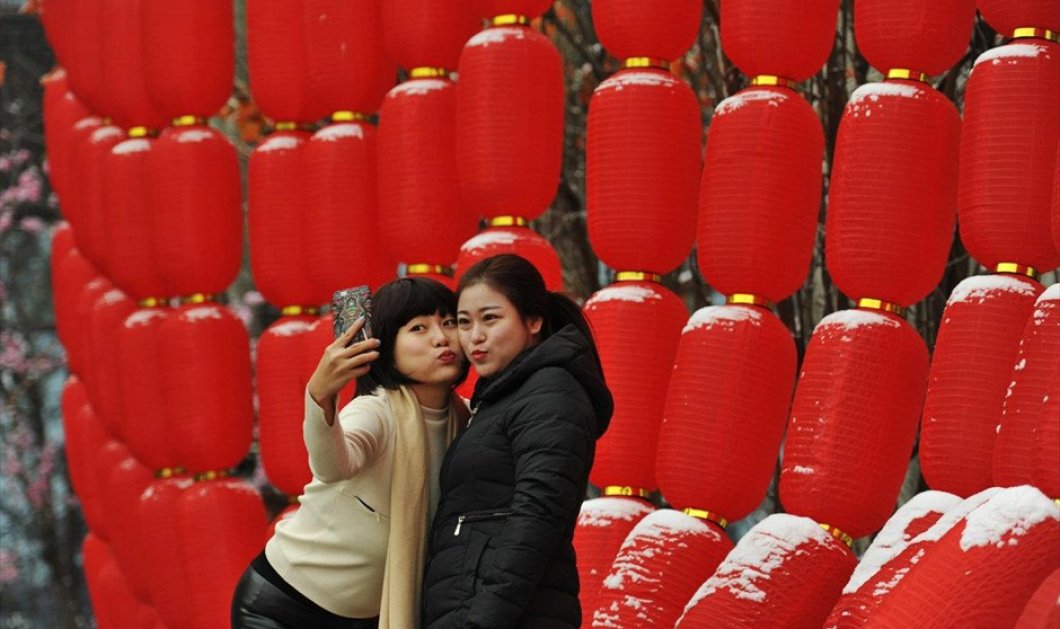 Δύο γυναίκες βγάζουν selfie σε κόκκινο φόντο, μετά το τέλος της χιονόπτωσης στην Τιεντζίν της Κίνας - Picture: REUTERS / CHINA STRINGER NETWORK 