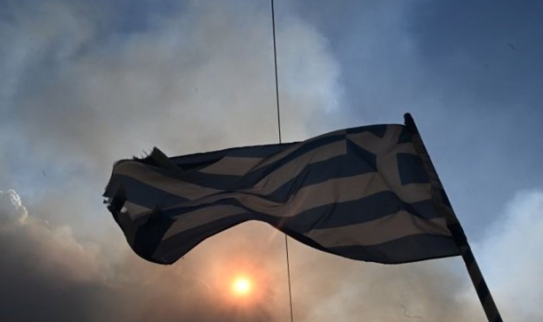 φωτό ημέρας η σημαία της Ελλάδας η οποία κυματίζει ανάμεσα στους καπνούς που άφησαν πίσω οι πυρκαγιές στην Αττική - eurokinissi